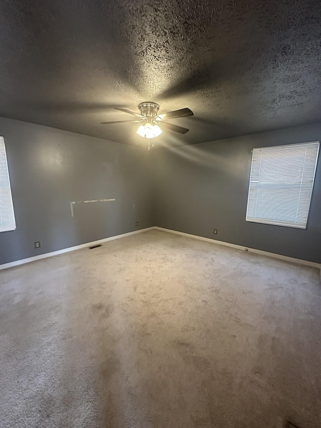 empty room featuring a textured ceiling, ceiling fan, and carpet