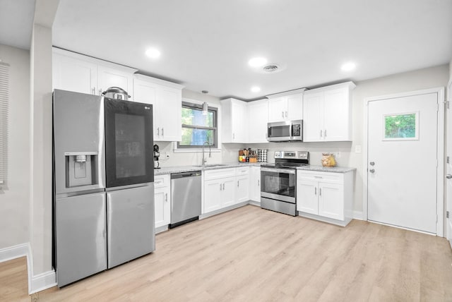 kitchen with appliances with stainless steel finishes, sink, white cabinets, light stone counters, and light hardwood / wood-style floors