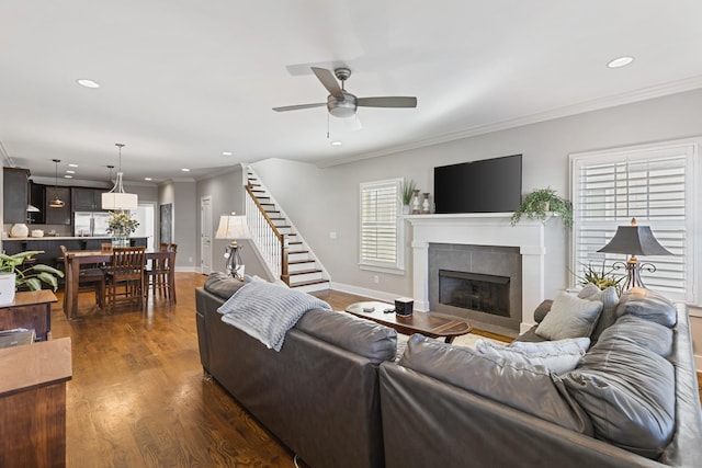 living room featuring dark wood-type flooring, ceiling fan, crown molding, and a tile fireplace