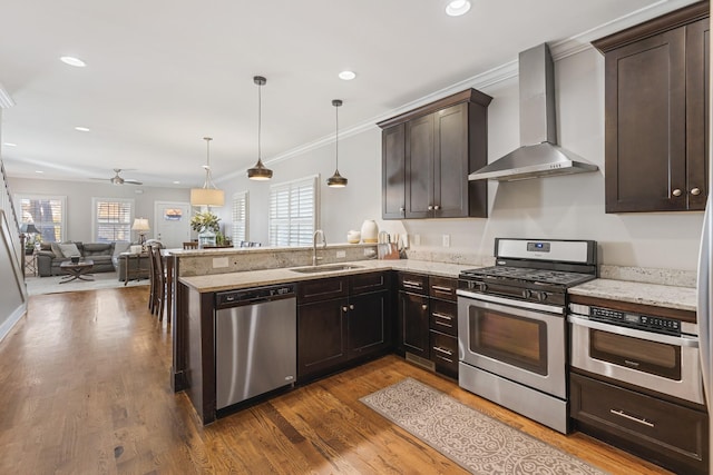 kitchen featuring appliances with stainless steel finishes, kitchen peninsula, hanging light fixtures, and wall chimney range hood