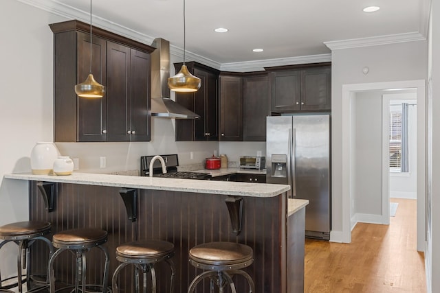 kitchen with stainless steel fridge with ice dispenser, dark brown cabinets, wall chimney range hood, and a kitchen bar