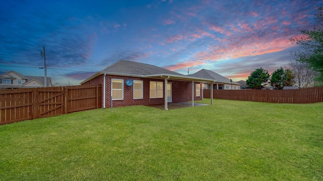 back house at dusk featuring a patio and a yard