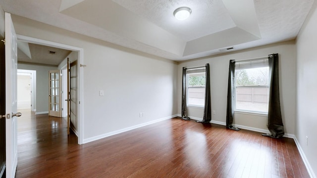 spare room with a textured ceiling, dark hardwood / wood-style flooring, and a tray ceiling