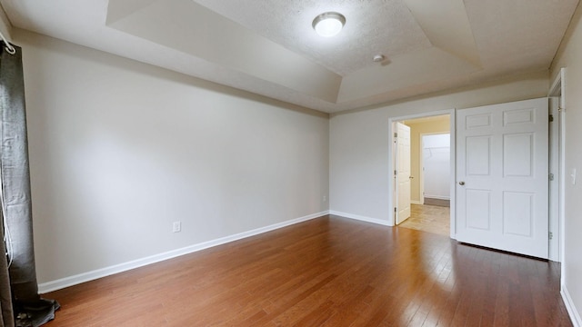 unfurnished bedroom with hardwood / wood-style floors, a tray ceiling, and a textured ceiling