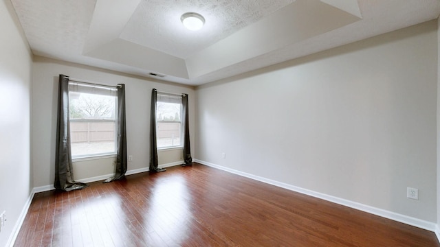 empty room featuring a raised ceiling, dark hardwood / wood-style floors, and a textured ceiling