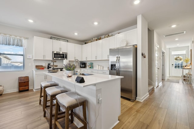 kitchen featuring white cabinetry, a center island with sink, light wood-type flooring, appliances with stainless steel finishes, and a kitchen breakfast bar