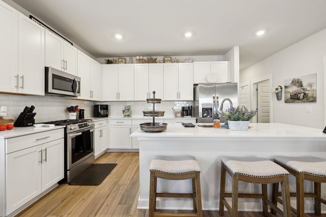 kitchen featuring white cabinetry, a kitchen breakfast bar, a kitchen island with sink, stainless steel appliances, and light hardwood / wood-style flooring