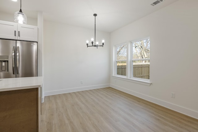 unfurnished dining area with an inviting chandelier and light hardwood / wood-style floors