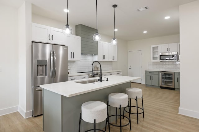 kitchen with sink, white cabinetry, decorative light fixtures, appliances with stainless steel finishes, and an island with sink