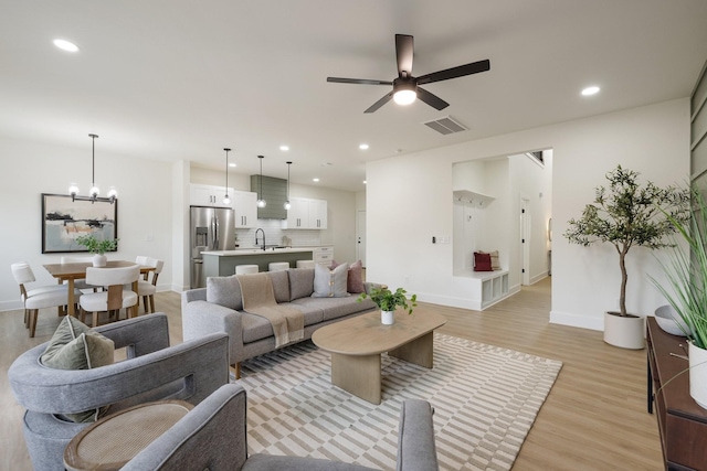 living room with sink, ceiling fan with notable chandelier, and light hardwood / wood-style floors