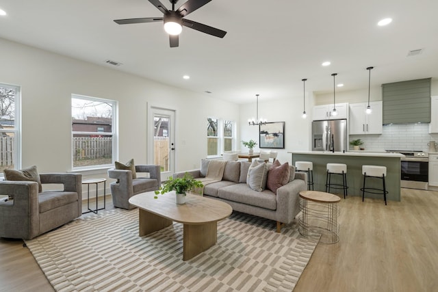 living room featuring ceiling fan with notable chandelier, plenty of natural light, and light hardwood / wood-style floors