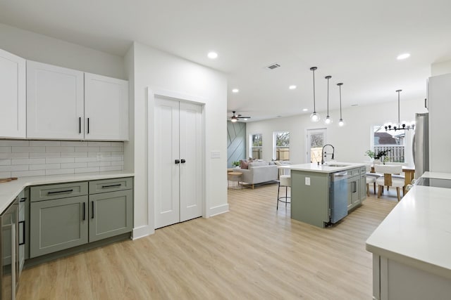 kitchen with sink, a center island with sink, light hardwood / wood-style flooring, appliances with stainless steel finishes, and pendant lighting