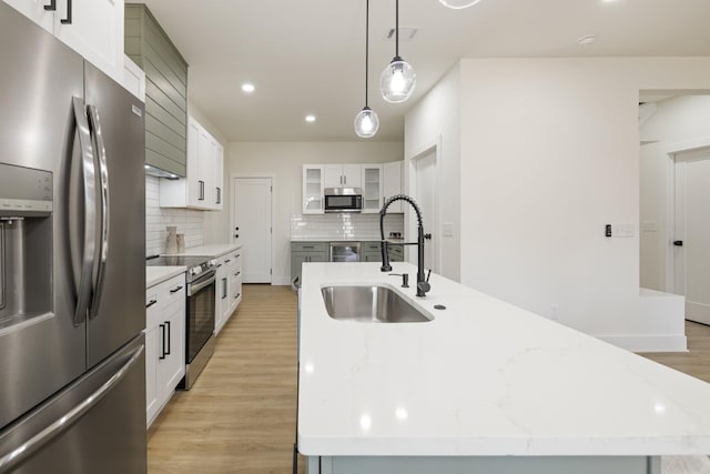 kitchen with pendant lighting, sink, a kitchen island with sink, white cabinetry, and stainless steel appliances