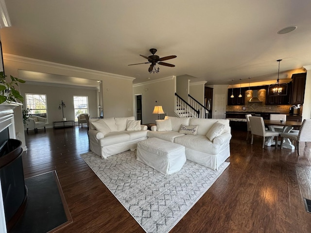 living room with ornamental molding, dark wood-type flooring, and ceiling fan with notable chandelier