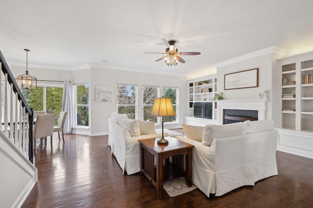 living room featuring dark hardwood / wood-style flooring, ceiling fan with notable chandelier, ornamental molding, and built in features