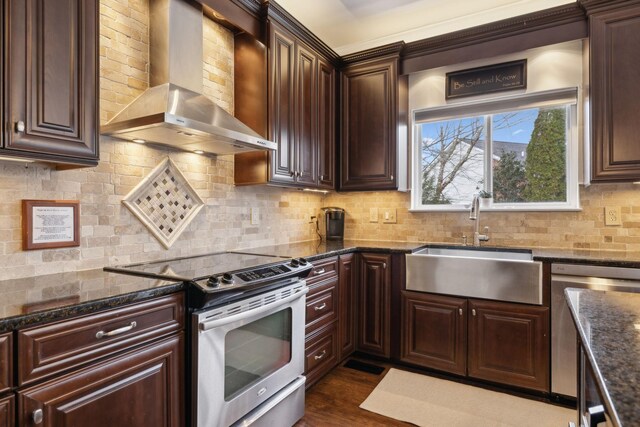 kitchen featuring wall chimney range hood, sink, stainless steel appliances, decorative backsplash, and dark stone counters