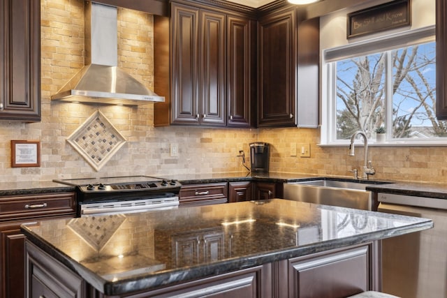 kitchen featuring appliances with stainless steel finishes, sink, backsplash, dark stone counters, and wall chimney range hood