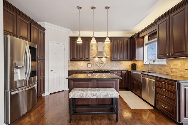 kitchen with wall chimney exhaust hood, sink, decorative light fixtures, appliances with stainless steel finishes, and a kitchen island