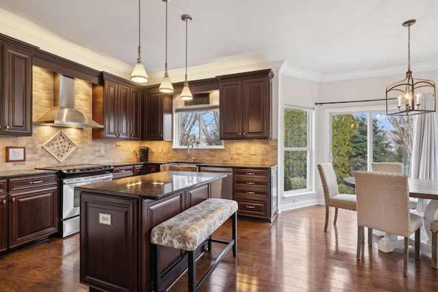 kitchen with a center island, hanging light fixtures, dark stone counters, stainless steel appliances, and wall chimney range hood