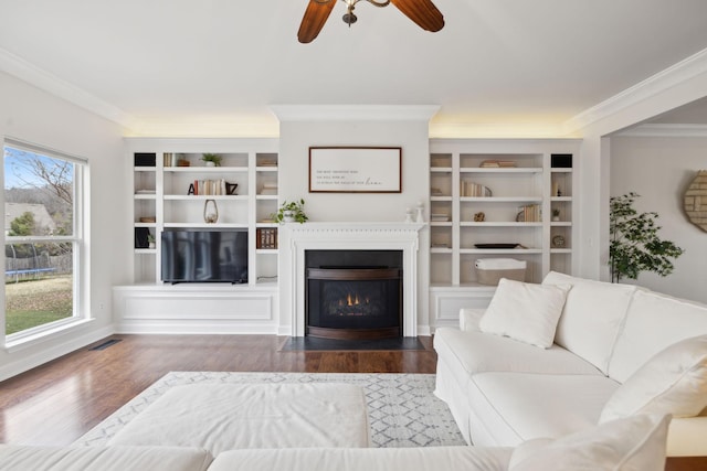 living room with wood-type flooring, ornamental molding, built in features, and ceiling fan