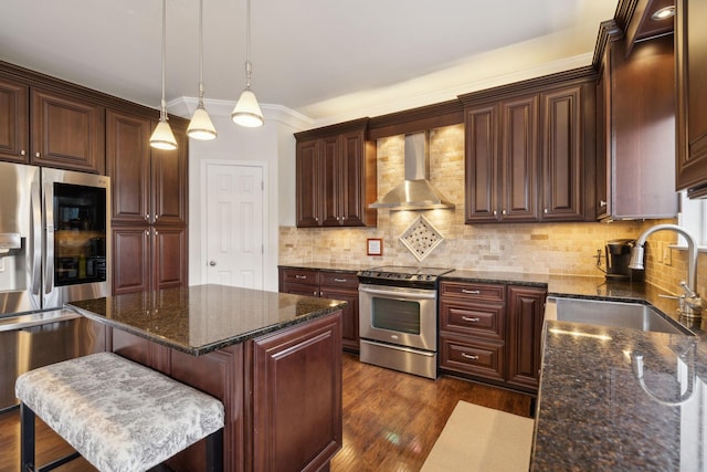 kitchen with wall chimney exhaust hood, a breakfast bar, sink, appliances with stainless steel finishes, and a kitchen island