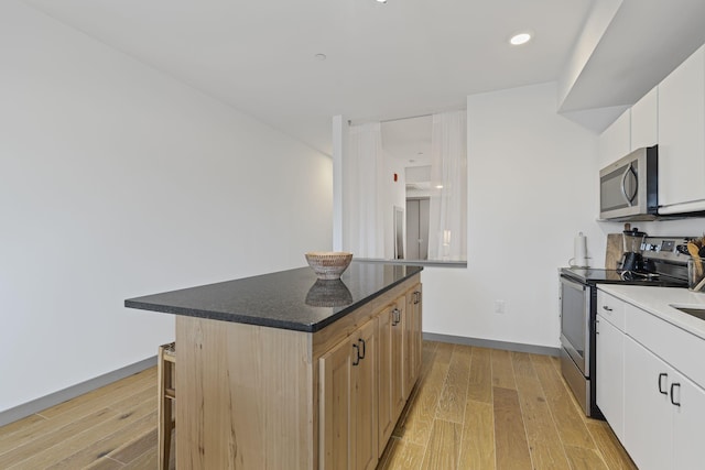 kitchen with stainless steel appliances, white cabinetry, a center island, and light wood-type flooring