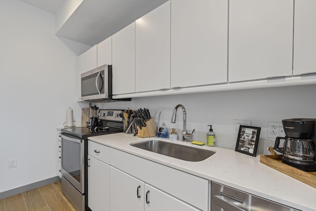 kitchen with white cabinetry, stainless steel appliances, sink, and light hardwood / wood-style flooring