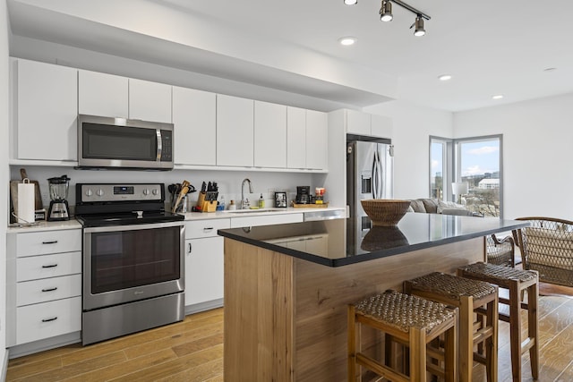 kitchen with appliances with stainless steel finishes, sink, white cabinets, a center island, and light hardwood / wood-style flooring