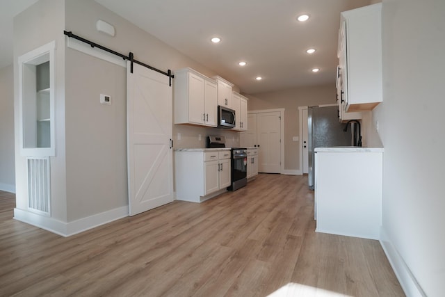 kitchen with white cabinetry, light stone counters, light hardwood / wood-style flooring, appliances with stainless steel finishes, and a barn door