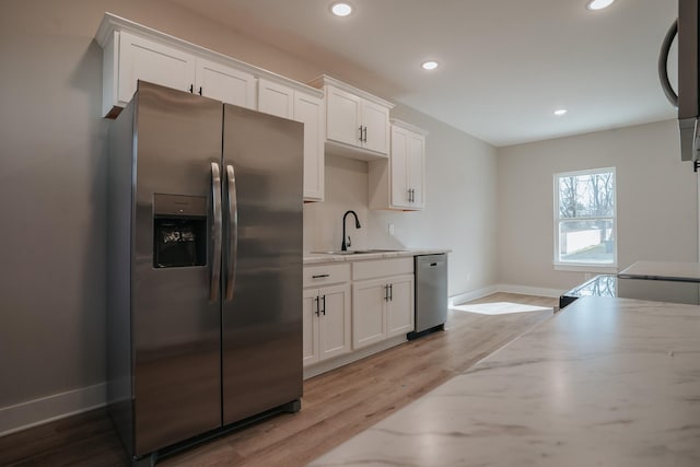 kitchen featuring white cabinetry, sink, stainless steel appliances, light stone countertops, and light wood-type flooring