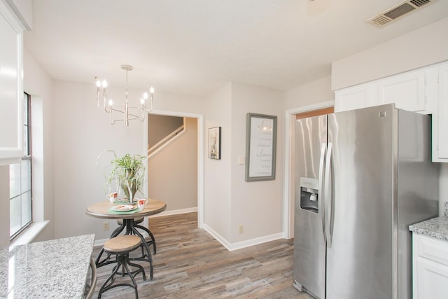 kitchen featuring pendant lighting, white cabinetry, stainless steel fridge, light stone counters, and light hardwood / wood-style floors