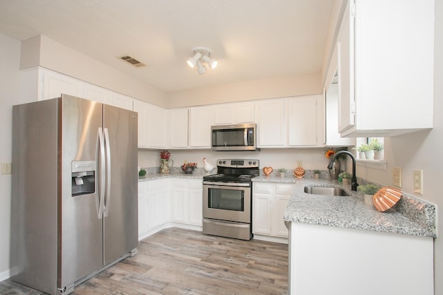 kitchen featuring sink, stainless steel appliances, light stone countertops, light hardwood / wood-style floors, and white cabinets