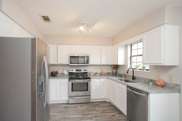 kitchen featuring sink, stainless steel appliances, light stone counters, wood-type flooring, and white cabinets