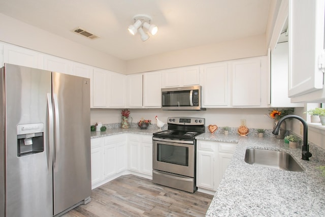 kitchen with appliances with stainless steel finishes, sink, white cabinets, light stone counters, and light hardwood / wood-style floors