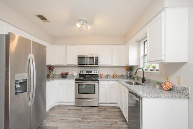 kitchen with stainless steel appliances, light stone countertops, sink, and white cabinets