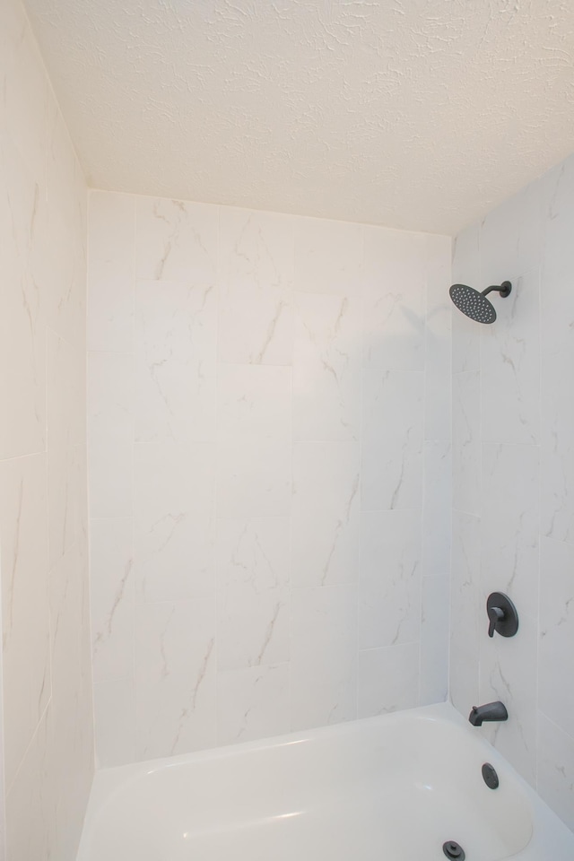 bathroom with tiled shower / bath combo and a textured ceiling