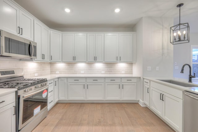 kitchen featuring sink, appliances with stainless steel finishes, white cabinets, decorative light fixtures, and light wood-type flooring