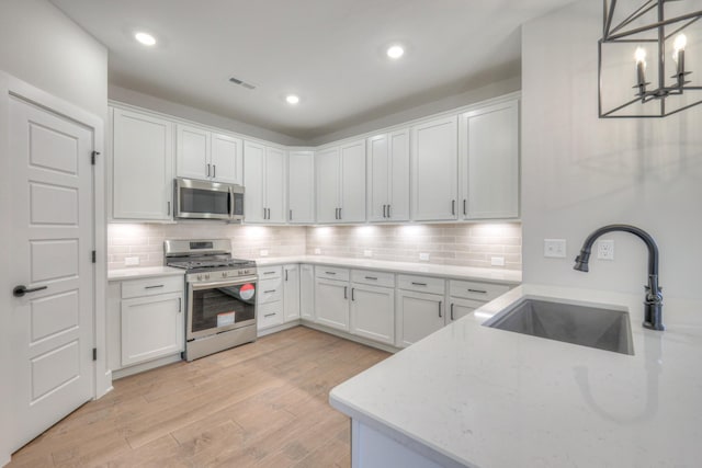 kitchen with sink, appliances with stainless steel finishes, pendant lighting, light stone countertops, and white cabinets