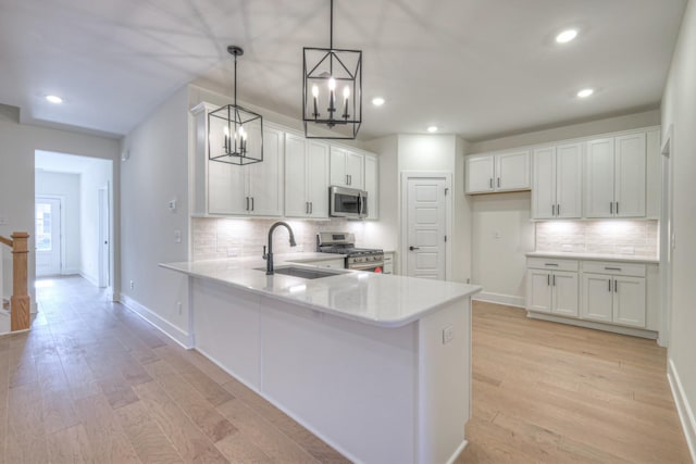 kitchen featuring sink, white cabinetry, decorative light fixtures, appliances with stainless steel finishes, and kitchen peninsula