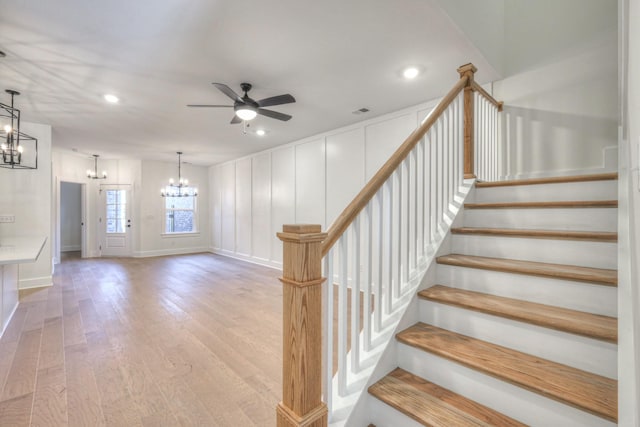 stairs featuring ceiling fan with notable chandelier and hardwood / wood-style floors