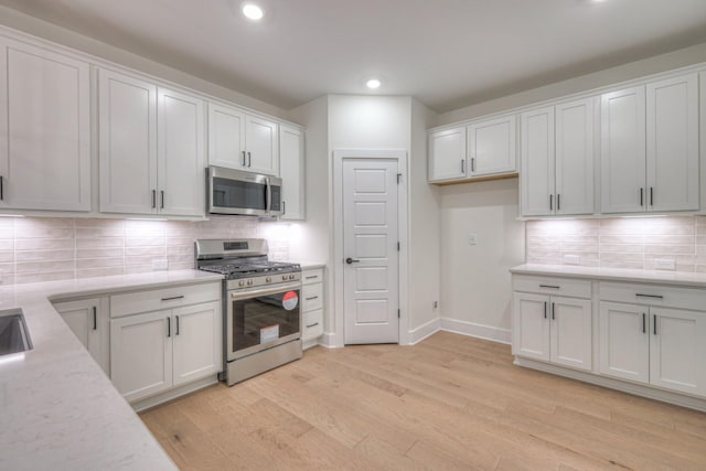 kitchen with decorative backsplash, appliances with stainless steel finishes, white cabinets, and light hardwood / wood-style flooring