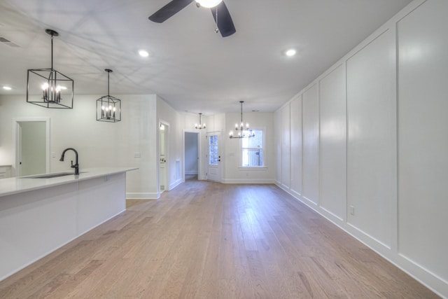 interior space with ceiling fan with notable chandelier, sink, pendant lighting, and light wood-type flooring