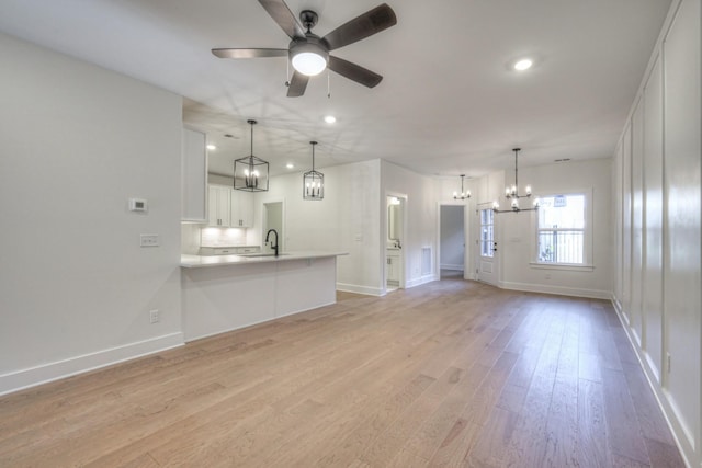 unfurnished living room with ceiling fan with notable chandelier, light hardwood / wood-style floors, and sink