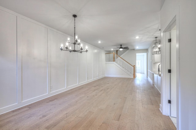 unfurnished dining area with ceiling fan with notable chandelier and light wood-type flooring