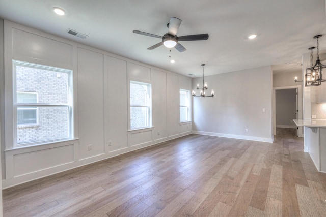 empty room with ceiling fan with notable chandelier and light hardwood / wood-style floors