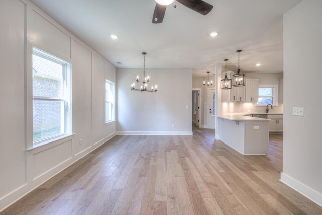 kitchen with white cabinetry, hanging light fixtures, tasteful backsplash, ceiling fan with notable chandelier, and light wood-type flooring