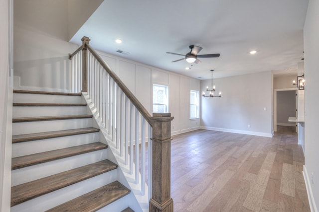 staircase with wood-type flooring and ceiling fan with notable chandelier