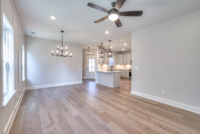 unfurnished living room featuring sink, ceiling fan with notable chandelier, and light wood-type flooring