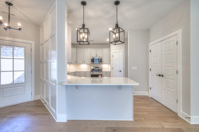 kitchen featuring decorative light fixtures, appliances with stainless steel finishes, kitchen peninsula, light hardwood / wood-style floors, and white cabinets