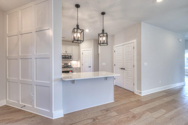 kitchen with appliances with stainless steel finishes, a breakfast bar area, white cabinets, hanging light fixtures, and light wood-type flooring